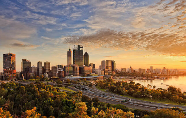 Gold warm sun light litting CBD of Perth city as seen from Kings park with green trees and highway entering in city
